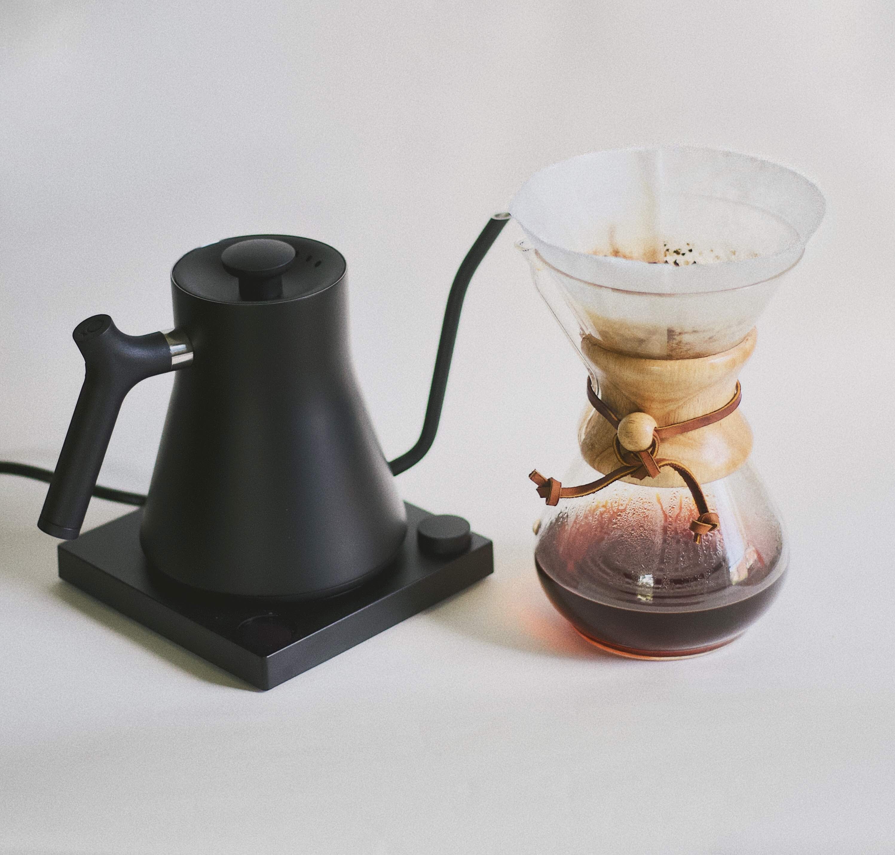 A black coffee pot on a burner next to a glass beaker with filter coffee inside.